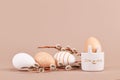 Simple natural colored Easter eggs with stripes and dots with bunny shaped egg cup and catkins on beige background Royalty Free Stock Photo