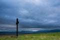 Simple oak catholic cross on green field, storm clouds over blue mountains Royalty Free Stock Photo