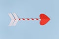 Simple paper cupid love arrow with heart shaped tip on blue background