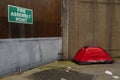 Simple red tent on a sidewalk of a street in a city. Homeless life in town. Social and poverty problem. Living in poverty