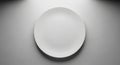 A simple, round, white ceramic plate centered on a smooth, gray surface. The background is evenly Royalty Free Stock Photo