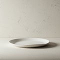 A simple round white ceramic plate is placed on a textured light-colored surface. The Royalty Free Stock Photo