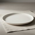 A simple, round, white ceramic plate rests on a light beige cloth napkin. The setting is Royalty Free Stock Photo