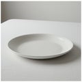 A simple, round, white ceramic plate rests on a white tablecloth. The setting emphasi Royalty Free Stock Photo