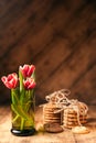 Simple rustic still life of red tulips in a green glass and stacks various cookies on wooden table.