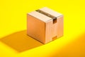 Simple sealed cardboard shipping box casting a soft shadow on a bright yellow background for delivery and packaging concepts Royalty Free Stock Photo