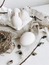 Simple Easter still life. Natural eggs, feathers, pussy willow branches, nest on white rustic table