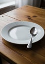 A simple table setting featuring a plain white ceramic plate with a shiny metal spoon Royalty Free Stock Photo