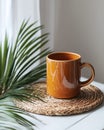 Simple terracotta mug on woven placemat, beside palm leaf Royalty Free Stock Photo