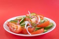 Simple vegetable salad of tomato, cucumber, onion and dill in white plate on bright red background.