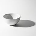 A simple, white ceramic bowl is placed against a plain white background. The bowl Royalty Free Stock Photo