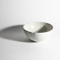 A simple white ceramic bowl is placed against a plain white background. The bowl is Royalty Free Stock Photo