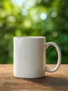 Plain white ceramic mug with handle placed on wooden surface against blurred green natural background for peaceful morning tea or Royalty Free Stock Photo