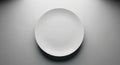 A simple white ceramic plate is positioned at the center of a plain gray surface. The lighting is Royalty Free Stock Photo
