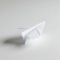 A simple, white paper airplane rests on a smooth, light gray surface. The airplane Royalty Free Stock Photo
