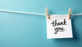 Simple white paper with cursive thank you message attached by wooden clothespins on a white string against a solid light blue Royalty Free Stock Photo