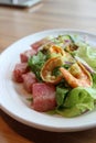 Simple white plate with seafood salad on bed of greens with chunks of watermelon on the side