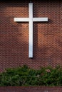 Simple white wooden cross on an exterior red brick wall, sunbeam on the wall