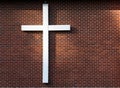 Simple white wooden cross on an exterior red brick wall, sunbeam on the wall