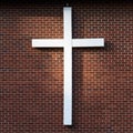 Simple white wooden cross on an exterior red brick wall, sunbeam on the wall