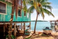 Simple wooden colorful house set on the wooden pillars next to the palm trees.