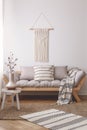 Simple, wooden stool on a wicker rug in a peaceful living room interior with a beautiful handmade decoration on a white wall