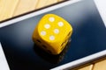 Simple yellow game dice showing six laying on a modern smartphone screen. Dice with 6 on it placed on a mobile phone display