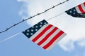 Simplified flag with American colors with red stripes and white stars on blue background hanging next to a barbed wire fence on bl