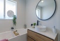 Simplistic modern bathroom with white walls, wooden drawers, and a round mirror