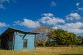 Simply design of public toilet in blue color surrounded by trees and green grass with clouds and blue sky in the background.