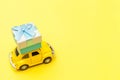 Simply design yellow vintage retro toy car delivering gift box on roof isolated on trendy yellow background. Christmas New Year
