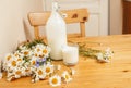 Simply stylish wooden kitchen with bottle of milk and glass on table, summer flowers camomile, healthy foog moring