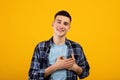 Sincere young guy putting hands on his heart, expressing gratitude on orange studio background Royalty Free Stock Photo