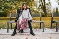 Sincerely laughing female dressed fashion boho style colorful long dress, warm knitted sweater with black leather biker jacket and