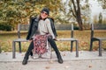 Sincerely laughing female dressed fashion boho style colorful long dress, warm knitted sweater with black leather biker jacket and