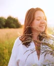 Sincerely smiling young pregnant woman dressed in light summer clothes walking by the high green grass meadow with wildflowers Royalty Free Stock Photo