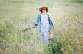 Sincerely smiling young Woman dressed jeans jacket and light summer dress walking by the high green grass meadow with basket and Royalty Free Stock Photo