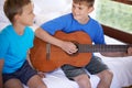 Sing with me. two bothers sitting on a bed with one playing a guitar. Royalty Free Stock Photo