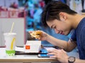 SINGAPORE - 18 MAR 2019 - Young Asian Chinese man eats a McDonalds meal while using his smartphone