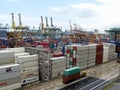 Transport truck moves two containers in the storage area. Dozens of stacked containers and large cranes in the background at the S