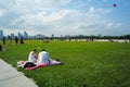 Singapore, Marina barrage-Couple of young people sit at the public outdoor park with people playing the kites in background