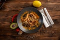 Singapore-style noodles with mushrooms and shrimps in a black plate on a wooden background