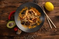 Singapore-style noodles with shiitake mushrooms and shrimps in a black plate on a wooden background