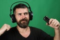 Singer with beard and winning face listens to music. Dj with beard wears headphones. Man holds microphone on green
