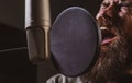 Singer with expressive face closeup wearing headphones is performing a song with a microphone while recording in a music