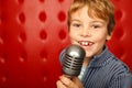 Singing boy with microphone on rack against red Royalty Free Stock Photo