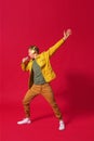 Singing young man enjoying song dancing with one hand up using phone and wireless headphones wearing jeans yellow jacket Royalty Free Stock Photo