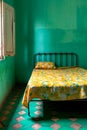 Single bed with yellow flowered blanket and blue wall behind it. Generative AI Royalty Free Stock Photo