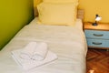 A single bed with yellow pillows and a white blanket in a room with yellow and green walls, a blue wooden bedside table Royalty Free Stock Photo