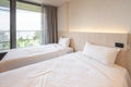 2 single beds with white bedding are in the cream bedroom of hotel that turn on the headboard light and open the gray curtain Royalty Free Stock Photo